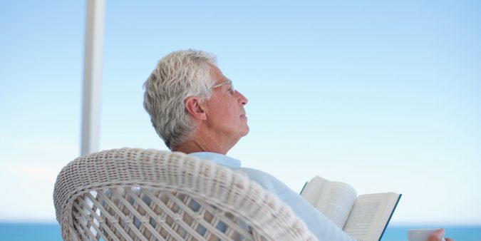 Senior man reading book on beach patio